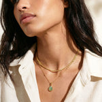 Gold layered necklaces with a green teardrop pendant on a person's neck
