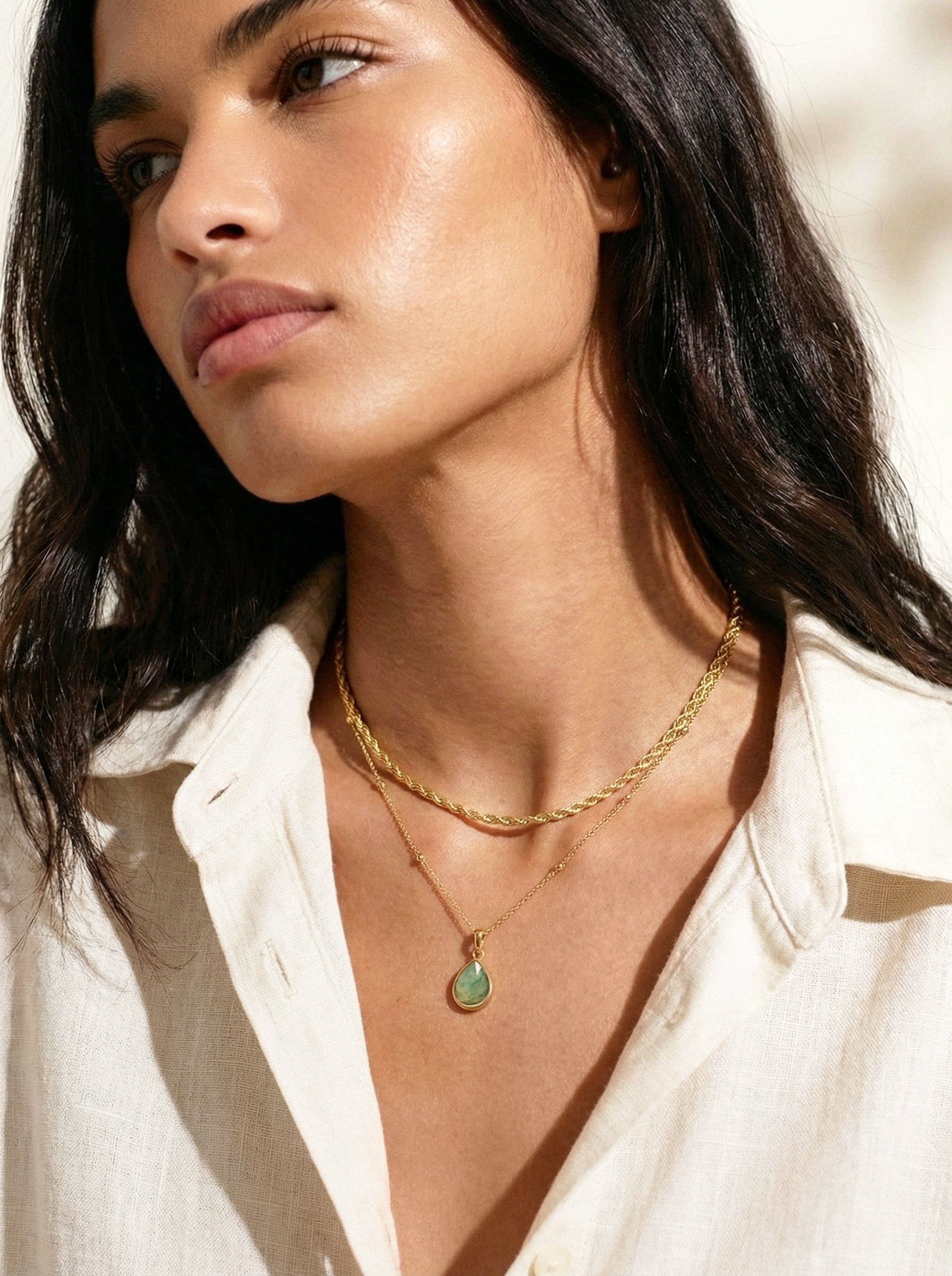 Gold layered necklaces with a green teardrop pendant on a person's neck