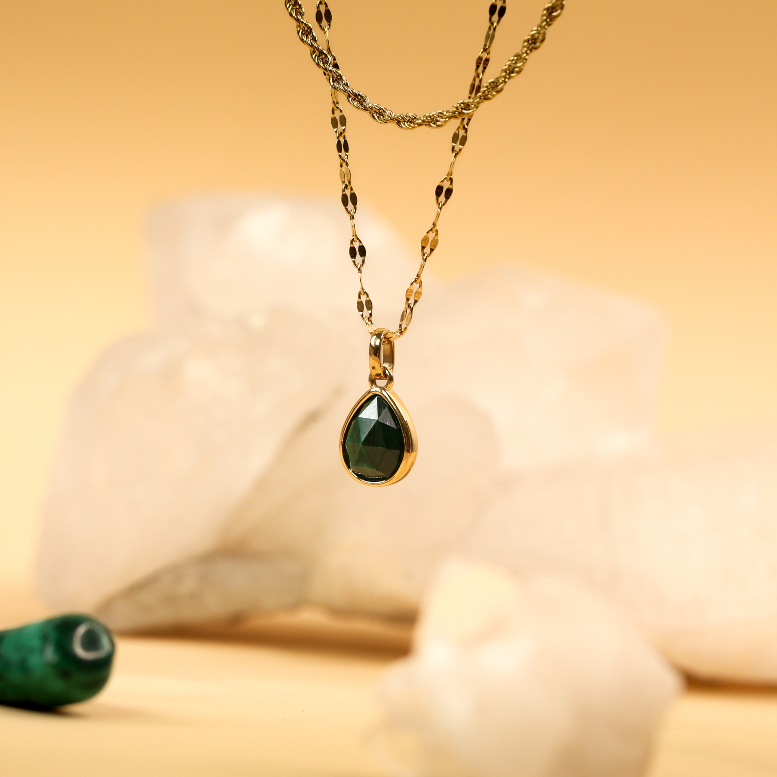 Gold necklace with a green teardrop pendant on a soft focus background