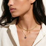 Woman wearing a gold necklace with a pendant against a neutral background