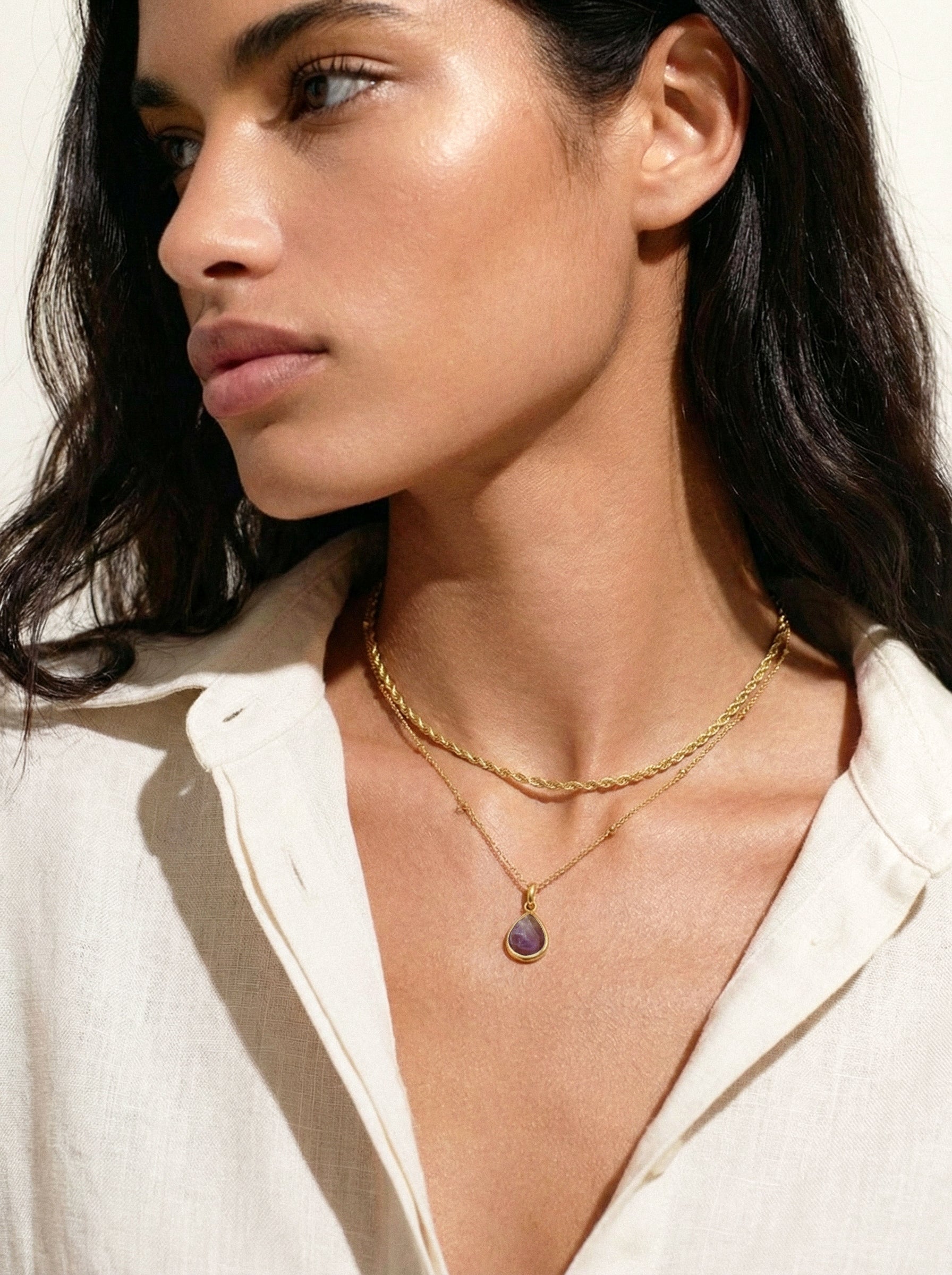 Woman wearing a gold necklace with a pendant against a neutral background