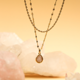 Gold necklace with a teardrop pendant on a soft background