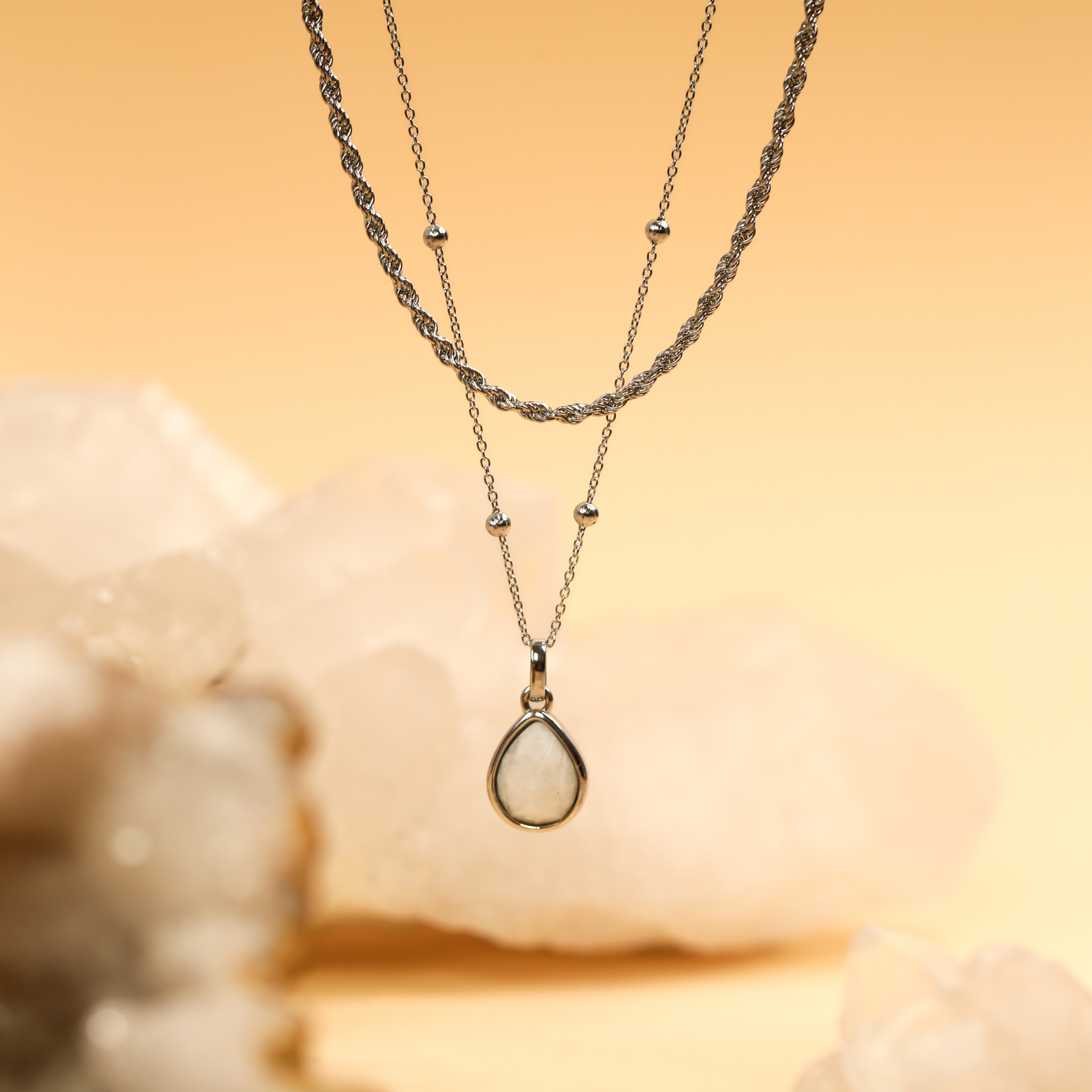 Two necklaces with teardrop pendants on a beige background