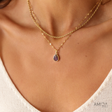 Gold necklace with a purple pendant on a person wearing a white top.