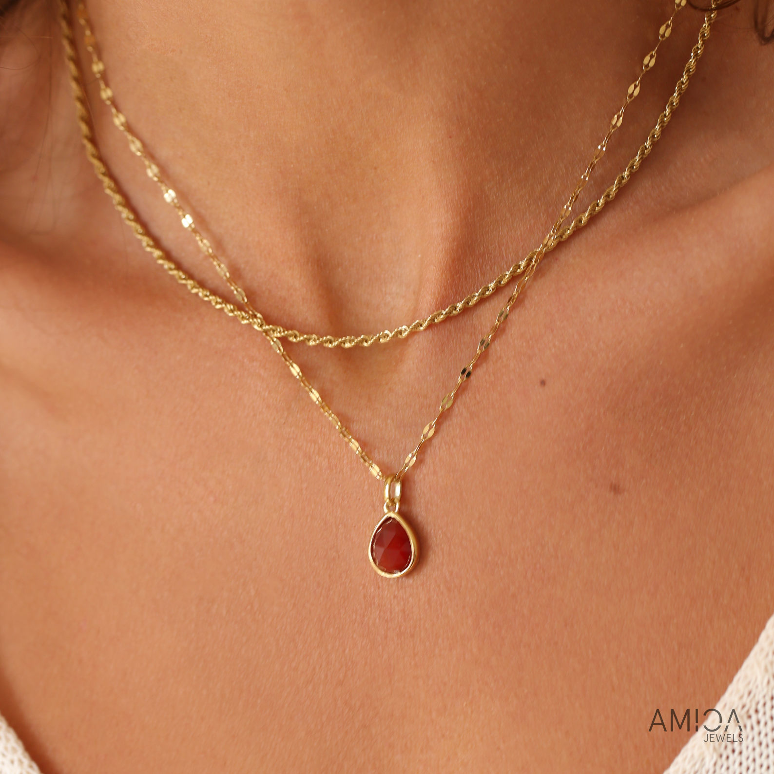 Gold necklace with a red pendant on a person's neck, brand 'AMiCA' visible