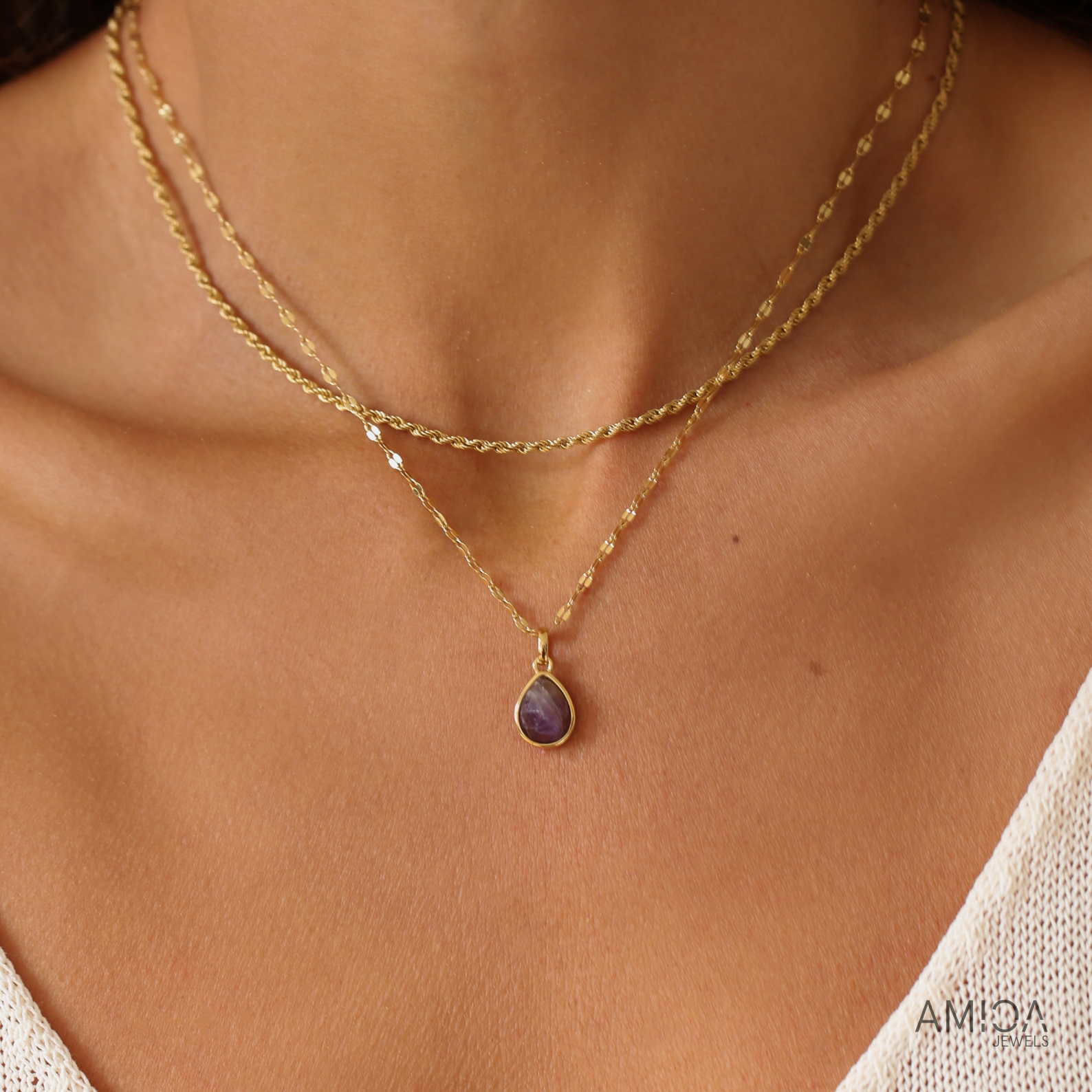 Gold necklace with a purple pendant on a person's neck, brand 'AMIDA' visible.