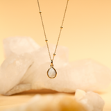 Gold necklace with a teardrop pendant on a soft yellow background