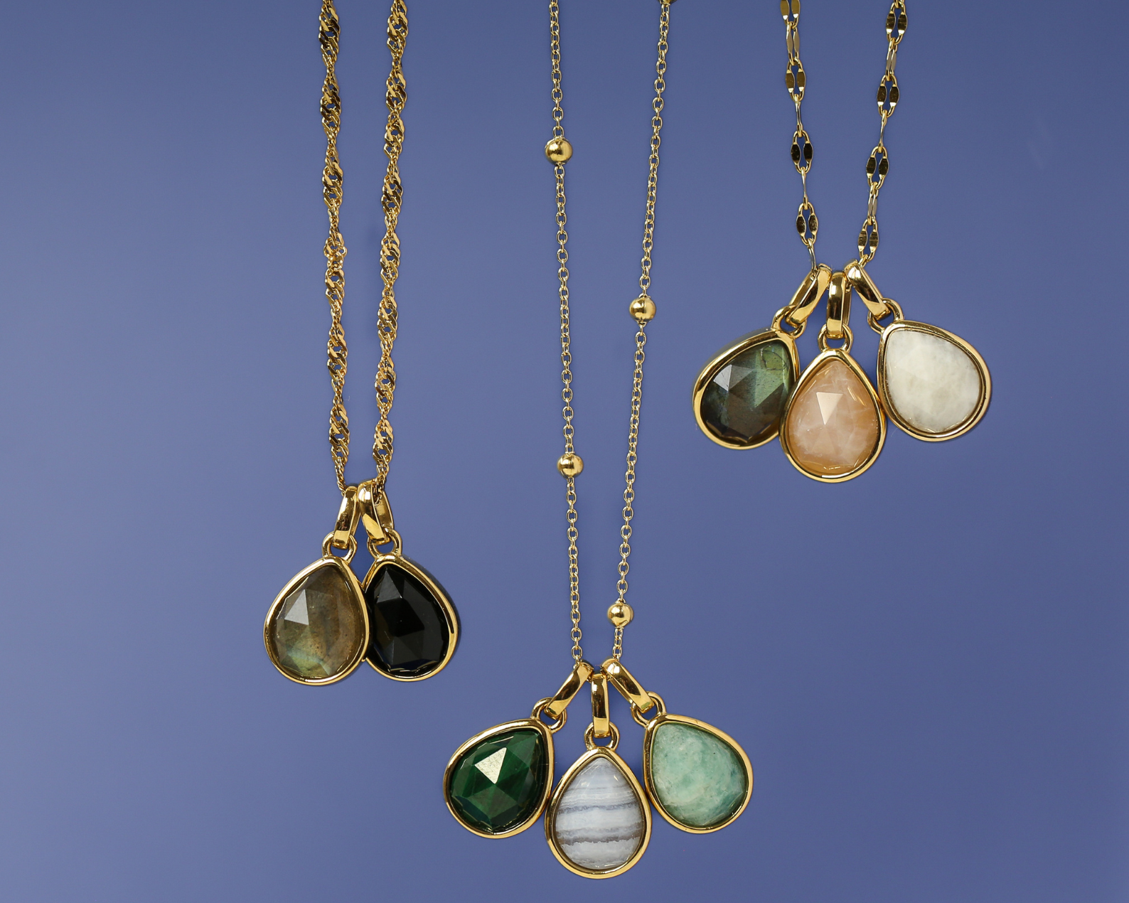 Three gold necklaces with teardrop-shaped gemstones on a blue background