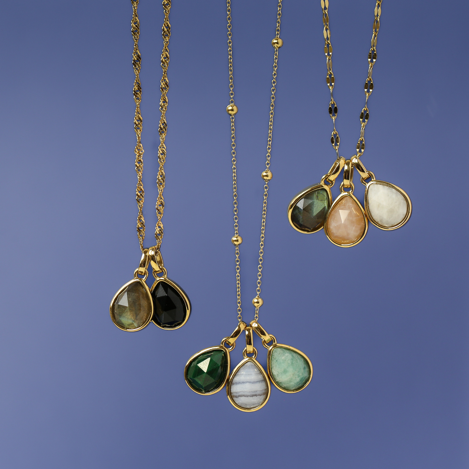 Three gold necklaces with teardrop-shaped gemstones on a blue background