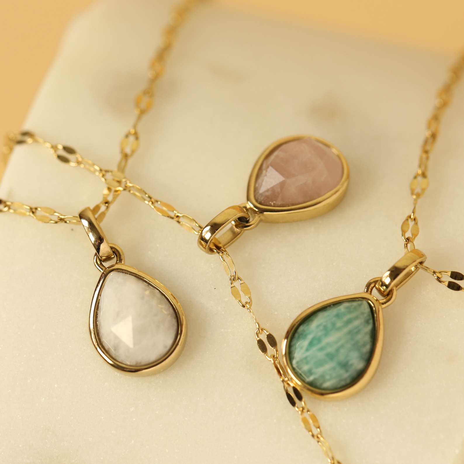Three gold necklaces with teardrop-shaped gemstones on a beige surface