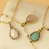 Three gold necklaces with teardrop-shaped gemstones on a beige surface