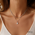 Close-up of a woman wearing a silver necklace with a teardrop pendant, branded 'AMICA JEWELERS'.