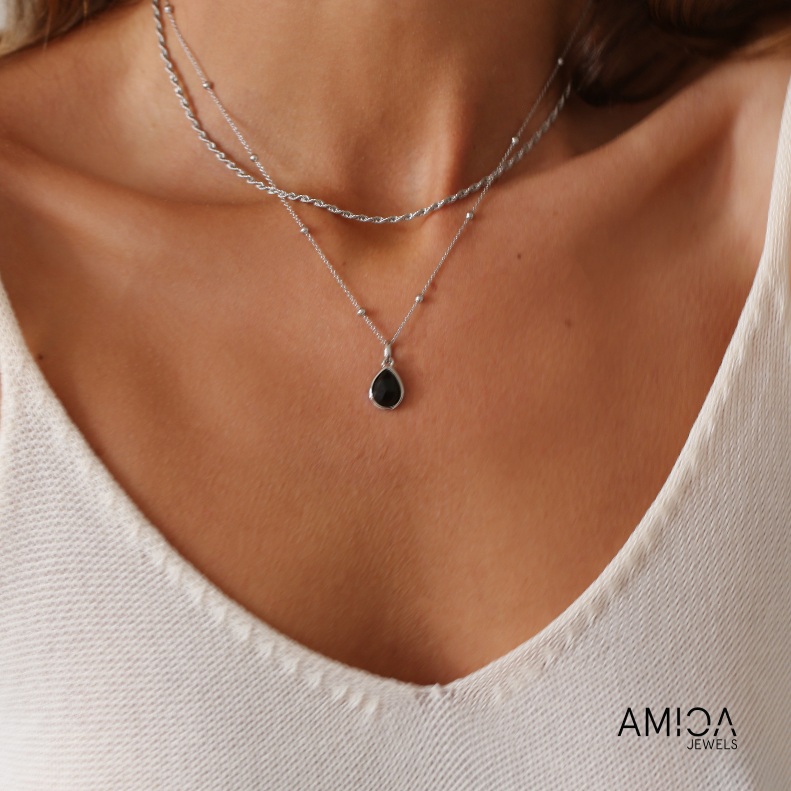 Necklace with a black pendant worn by a person, with 'Amica Jewels' branding.