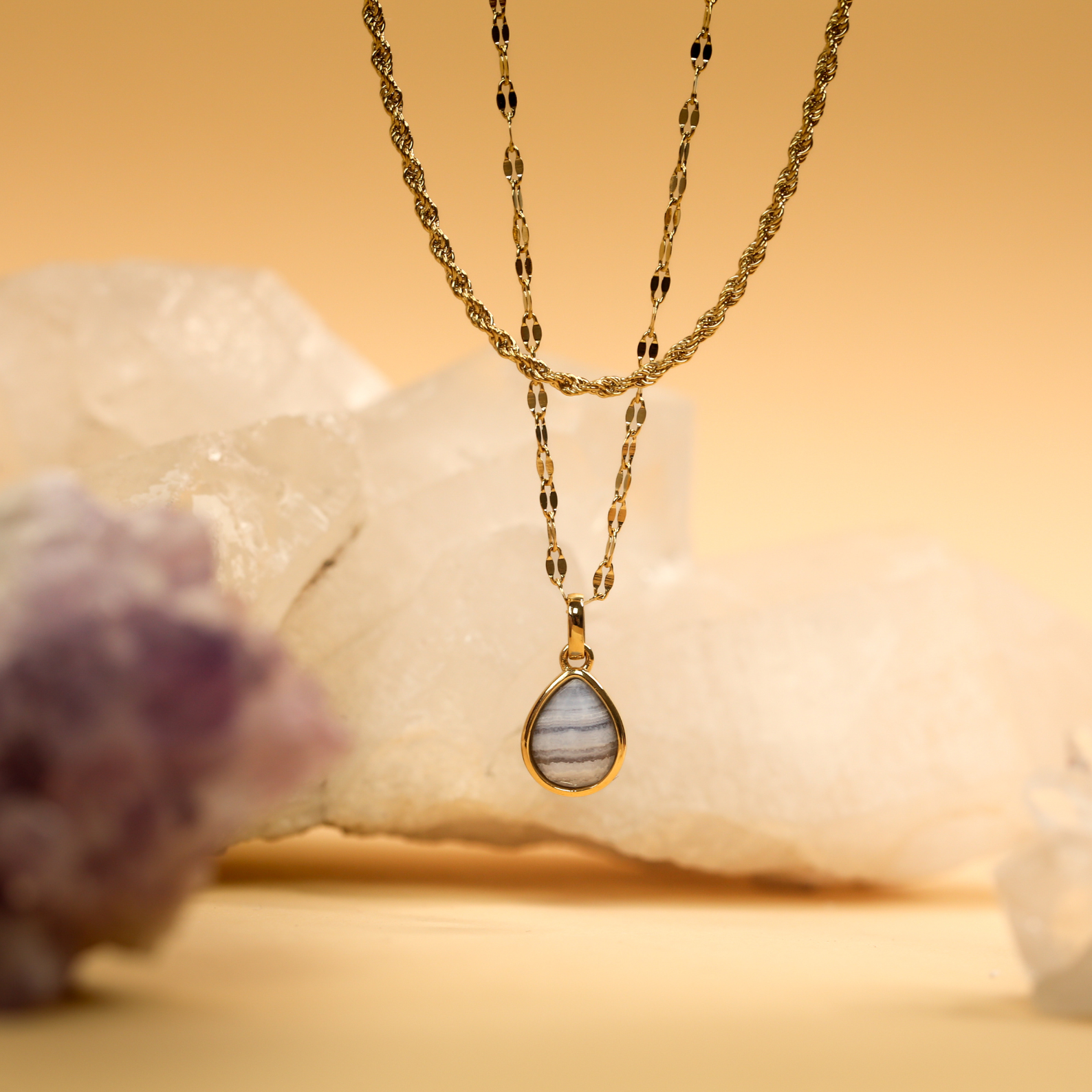 Gold necklace with a teardrop pendant on a stone background