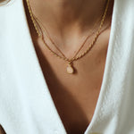 Close-up of a person wearing a gold necklace with a small pendant on a white background
