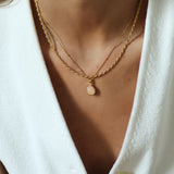 Close-up of a person wearing a gold necklace with a small pendant on a white background