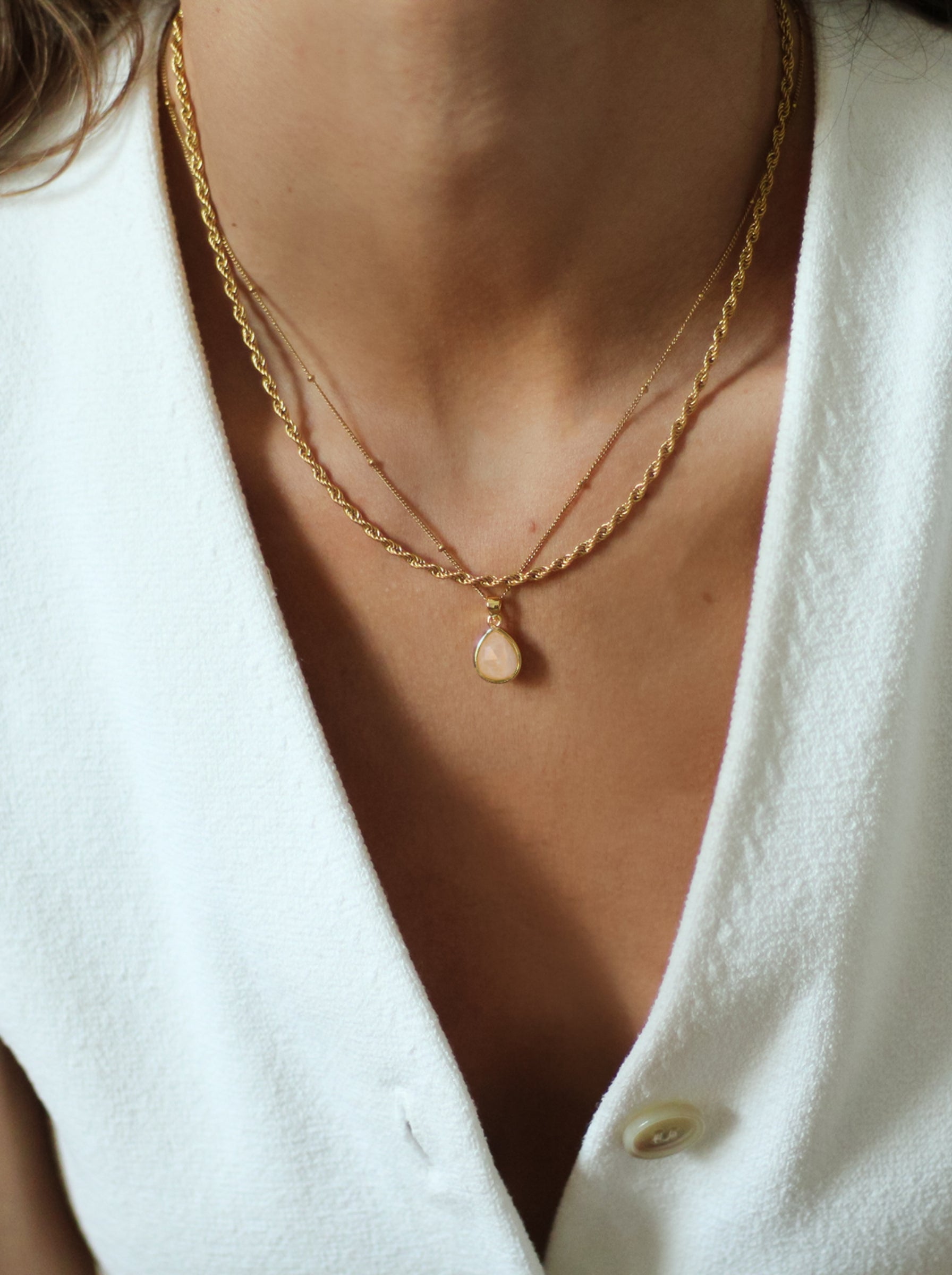 Close-up of a person wearing a gold necklace with a small pendant on a white background