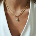 Close-up of a person wearing a gold necklace with a teardrop pendant on a white background.