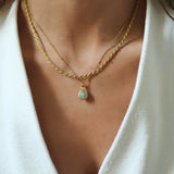 Close-up of a person wearing a gold necklace with a teardrop pendant on a white background.