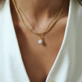 Close-up of a person wearing a gold necklace with a pendant, set against a white background.