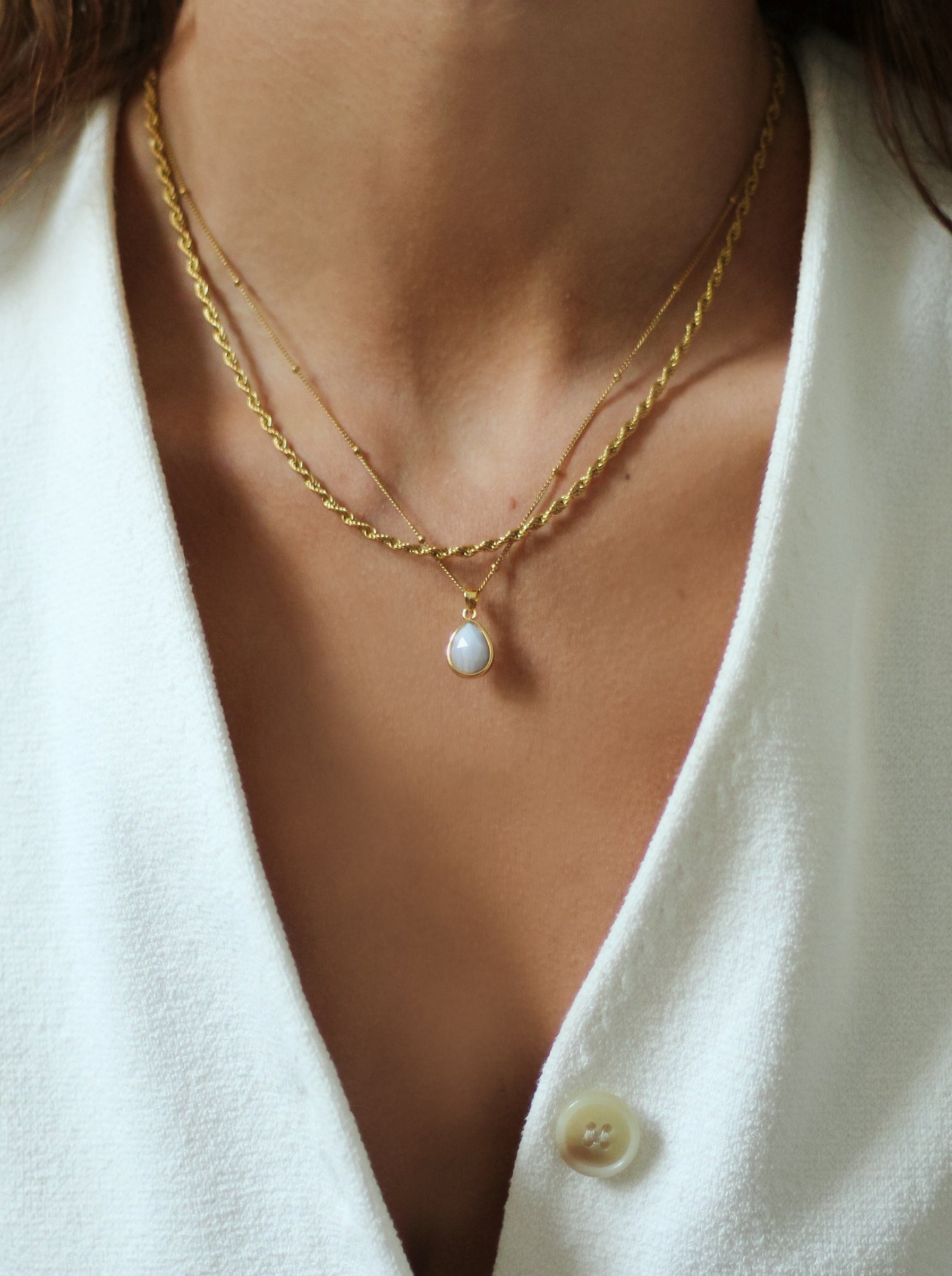 Close-up of a person wearing a gold necklace with a pendant, set against a white background.
