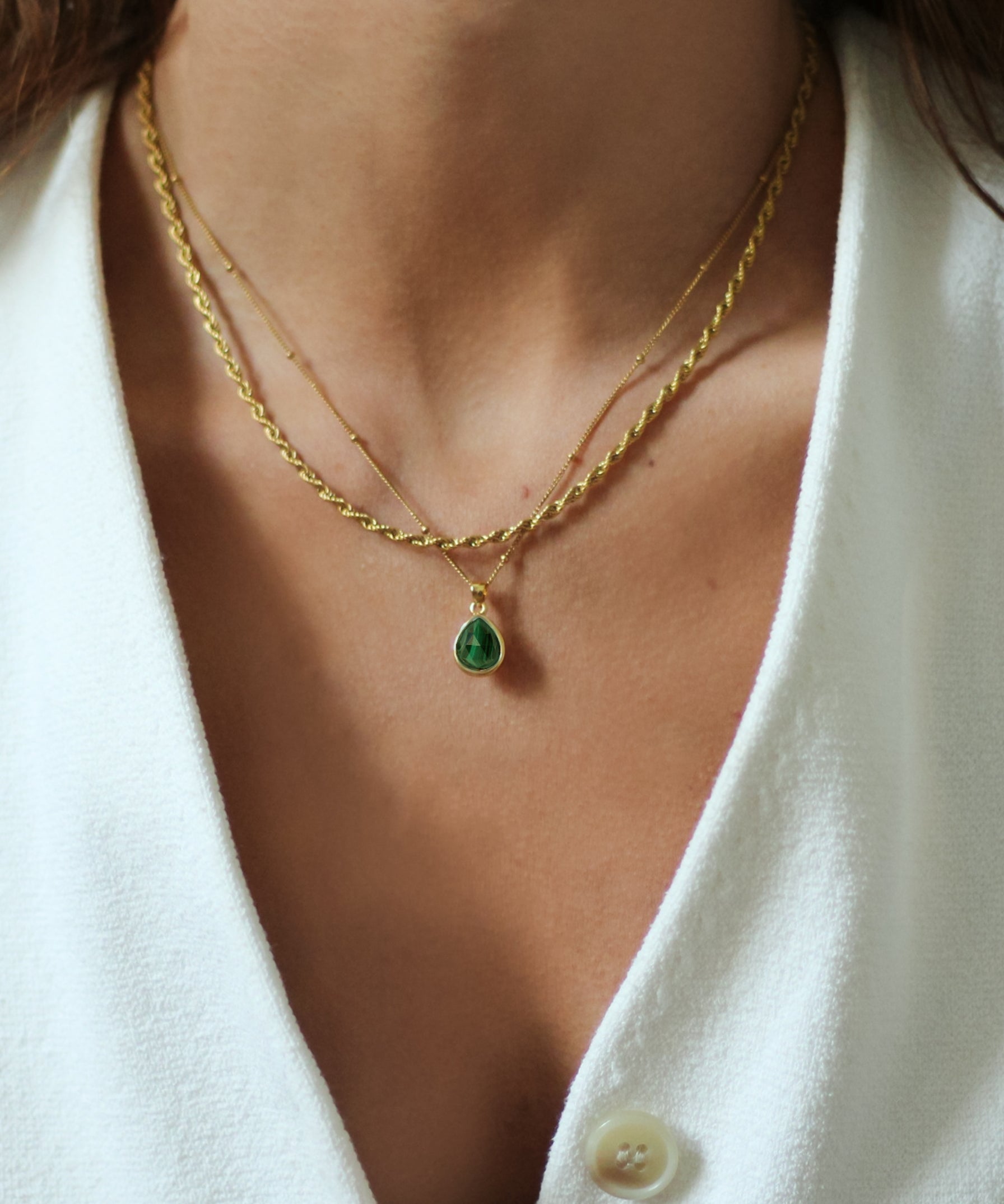 Close-up of a person wearing a gold necklace with a pendant on a white background