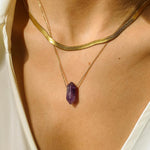 Natural Amethyst crystal necklace. The first necklace features a pointed amethyst crystal pendant, while the second necklace features a delicate gold snake chain. Together, the necklaces create a stunning layered look that adds sophistication and elegance to any outfit.