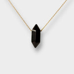 Black obsidian crystal necklace. The necklace features a pointed black obsidian crystal pendant attached to a gold chain, creating a stunning and eye-catching piece of jewelry.