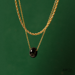 Gold chain necklace with a black pendant on a green background