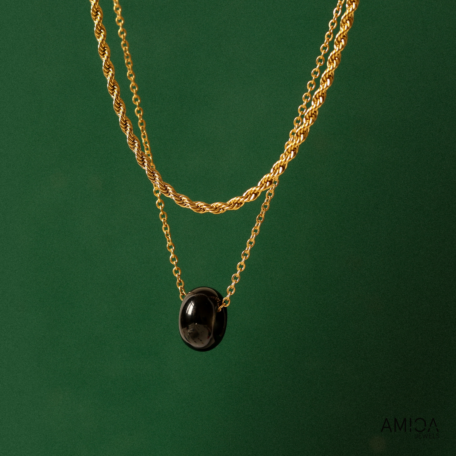 Gold chain necklace with a black pendant on a green background