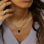Close-up of a person wearing a gold necklace with a black pendant.
