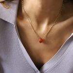 Necklace with a red pendant worn by a person in a light gray top.