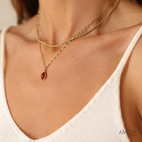 Gold necklace with a red pendant worn by a person in a white top, with 'AMICA' brand visible.