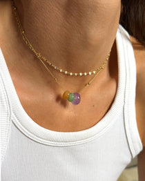 Gold necklace with yellow, green, and purple gemstone charms over a white ribbed top