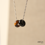 Necklace with two round beads on a beige background, featuring the brand 'AMICA JEWELS'.