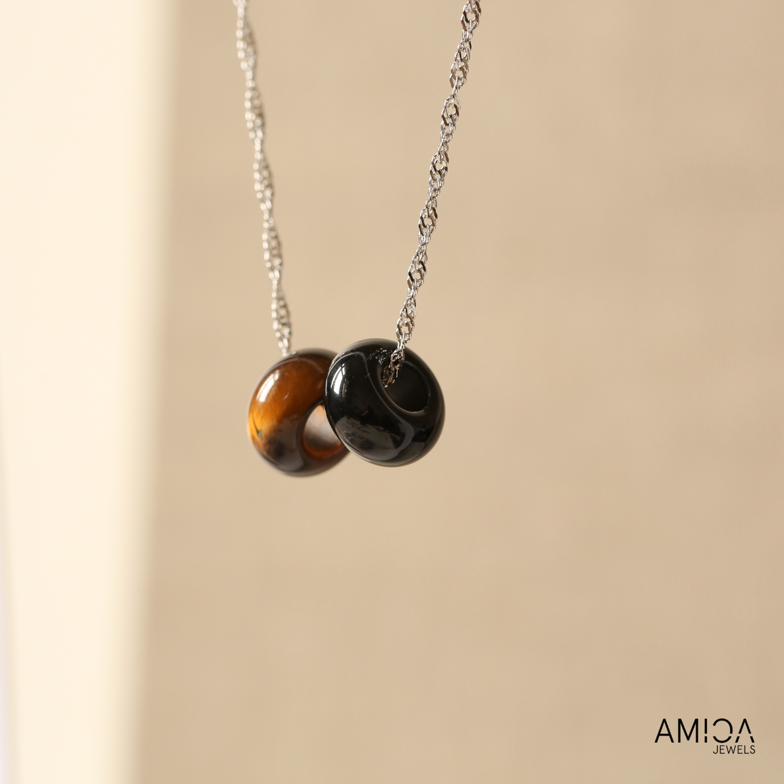 Necklace with two round beads on a beige background, featuring the brand 'AMICA JEWELS'.