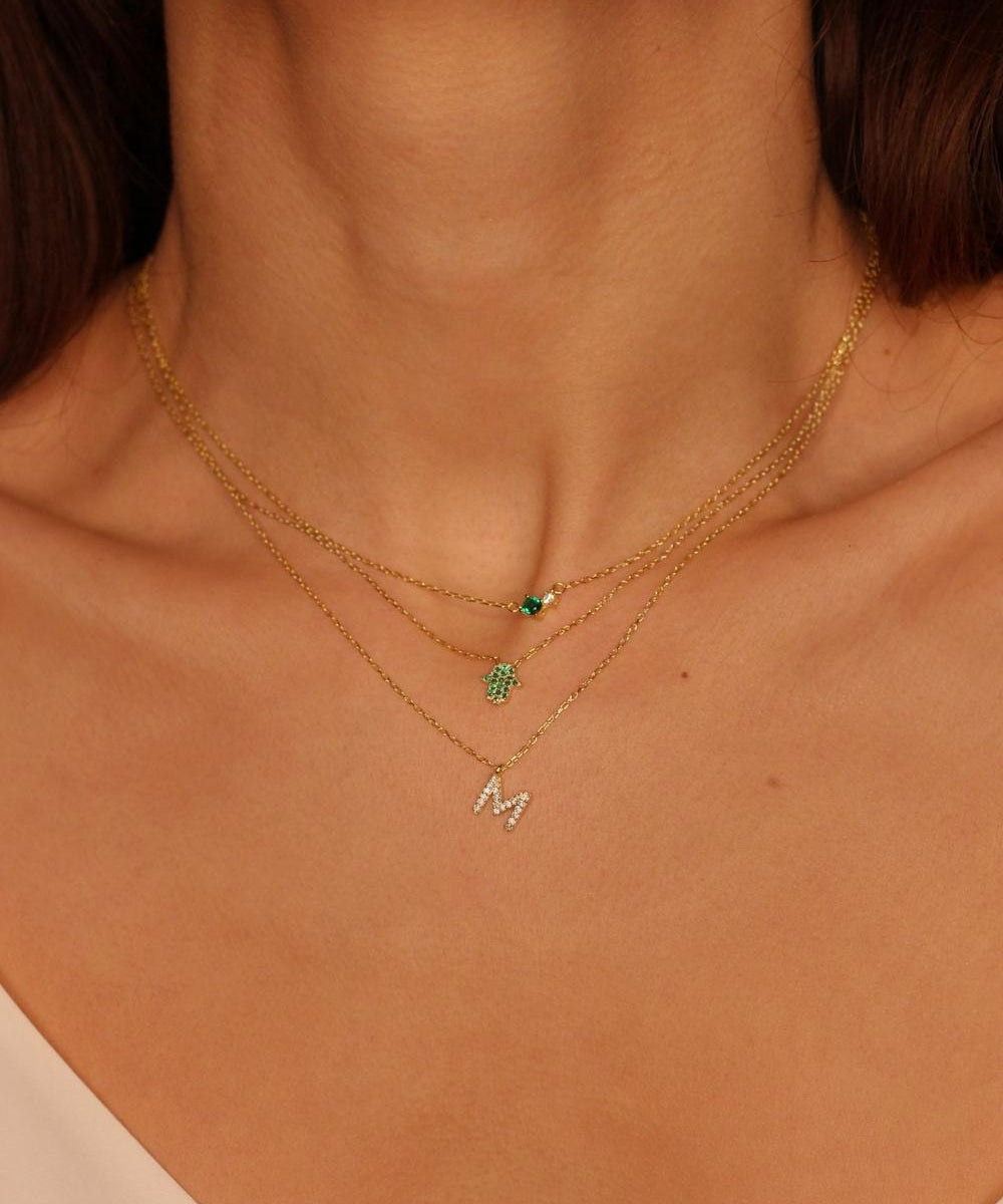 A Green Hamsa hand charm necklace in 18k gold plated silver. The necklace features a delicate chain with a beautifully designed Hamsa hand charm pendant. The Hamsa hand symbol is believed to bring protection, good luck, and ward off evil. The necklace is designed to be worn comfortably and can be adjusted to fit different neck sizes.