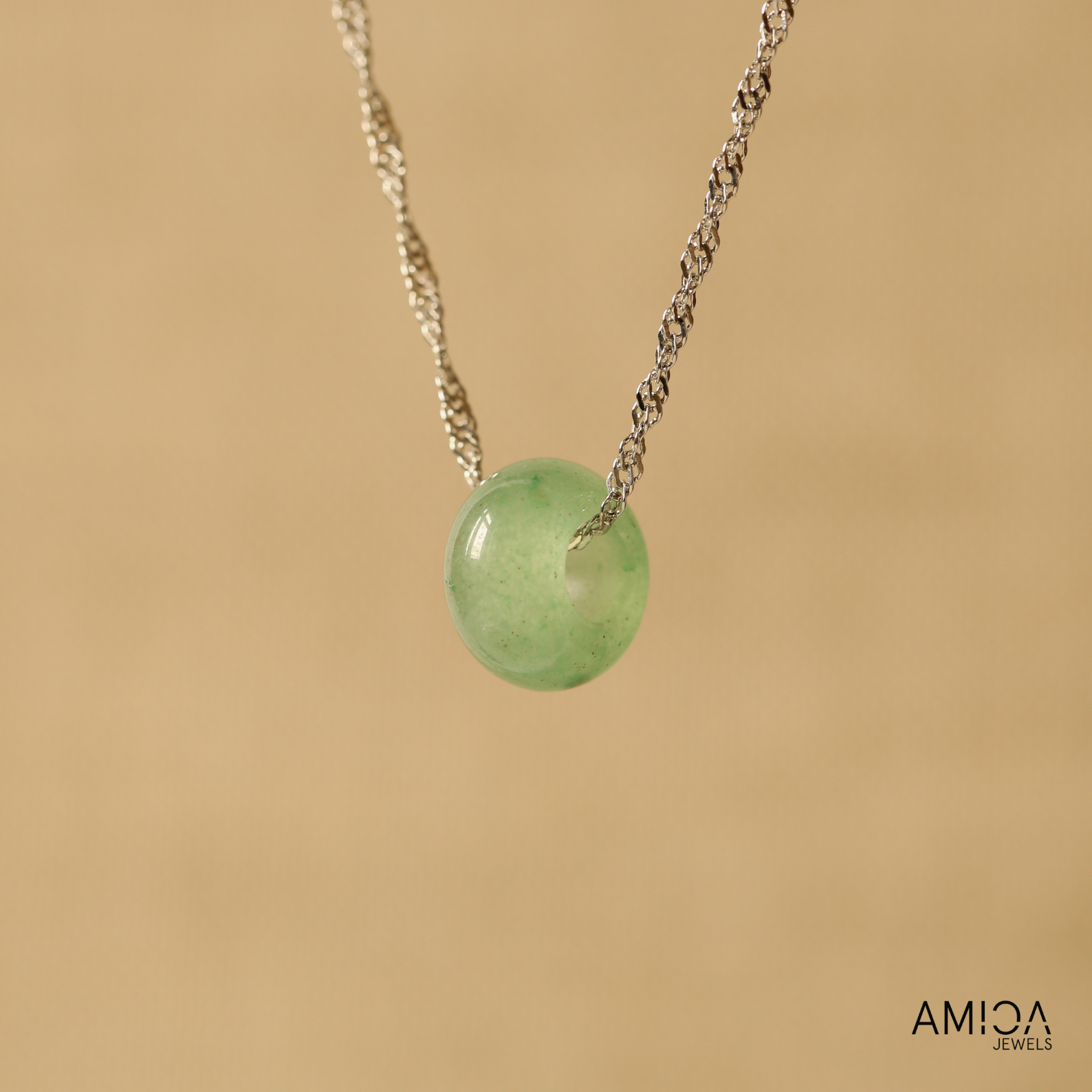 Necklace with a green pendant on a beige background, featuring the brand 'AMICA JEWELS'.