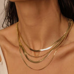 A layered set of herringbone flat chains in 18k gold plated. The set includes multiple flat chains with a distinct herringbone pattern, all crafted in a luxurious gold color. The chains are layered together, creating a stylish and modern look. The herringbone pattern adds a unique texture and visual interest to the chains, while the gold color adds a touch of glamour