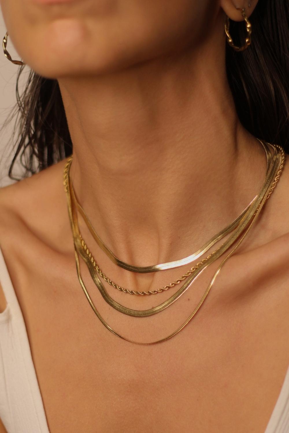 A layered set of herringbone flat chains in 18k gold plated. The set includes multiple flat chains with a distinct herringbone pattern, all crafted in a luxurious gold color. The chains are layered together, creating a stylish and modern look. The herringbone pattern adds a unique texture and visual interest to the chains, while the gold color adds a touch of glamour