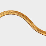 A detail of herringbone flat chain in 18k gold plated. The chain features a distinct herringbone pattern with flat, interlocking links that create a sleek and polished appearance. The gold color adds a touch of luxury and elegance to the chain. The herringbone flat chain is a versatile accessory that can be worn on its own as a statement piece or layered with other necklaces for a stylish and trendy look. This chain is perfect for both casual and formal occasions, adding a touch of glamour to any outfit.