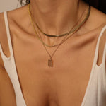 A layered set of herringbone flat chains in 18k gold plated. The set includes three gold chains with a distinct herringbone pattern, all crafted in a luxurious gold color. The chains are layered together, creating a stylish and modern look. The herringbone pattern adds a unique texture and visual interest to the chains, while the gold color adds a touch of glamour