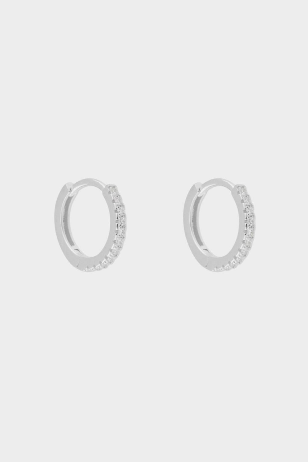 diamond huggie hoops in sterling silver. The earrings feature a classic huggie-style design adorned with sparkling diamonds. The diamonds are meticulously set along the front of the hoops, adding a touch of luxury and glamour. The hoops are made of high-quality silver and have a polished finish.