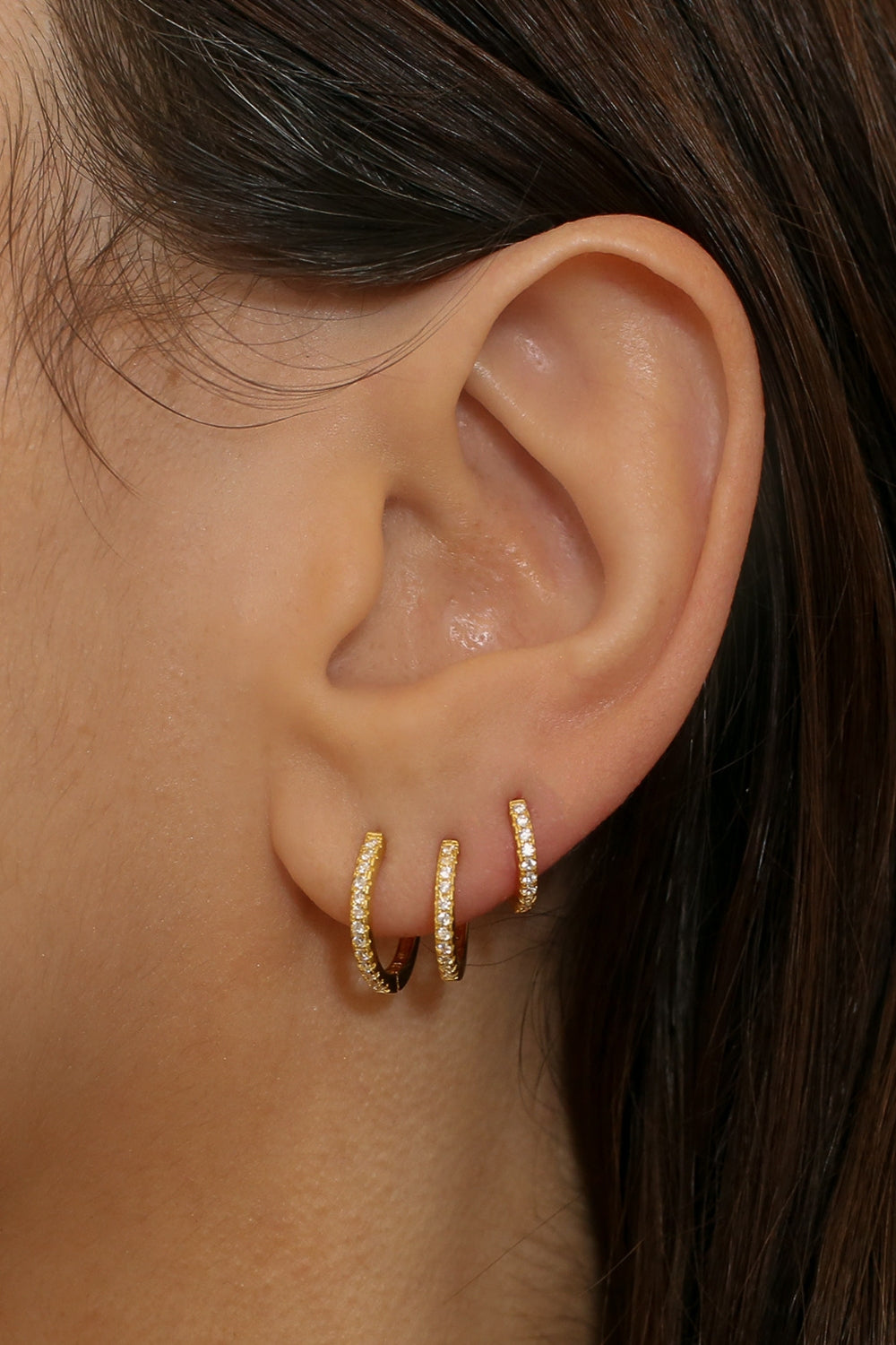 diamond huggie hoops in 18k gold plated silver. The earrings feature a classic huggie-style design adorned with sparkling diamonds. The diamonds are meticulously set along the front of the hoops, adding a touch of luxury and glamour. The hoops are made of high-quality gold plated silver and have a polished finish.