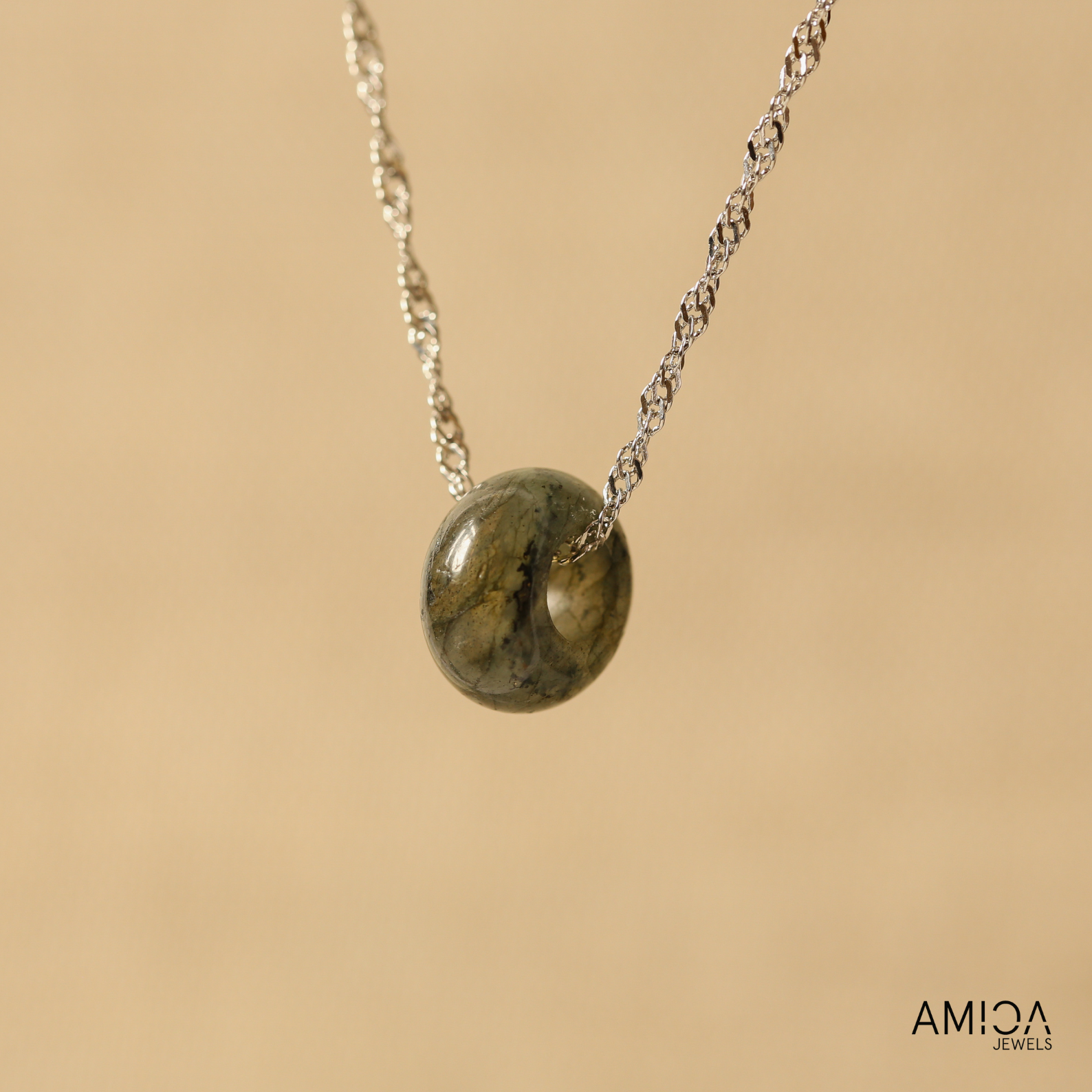 Necklace with a green stone pendant on a beige background, featuring the brand 'AMICA JEWELS'.