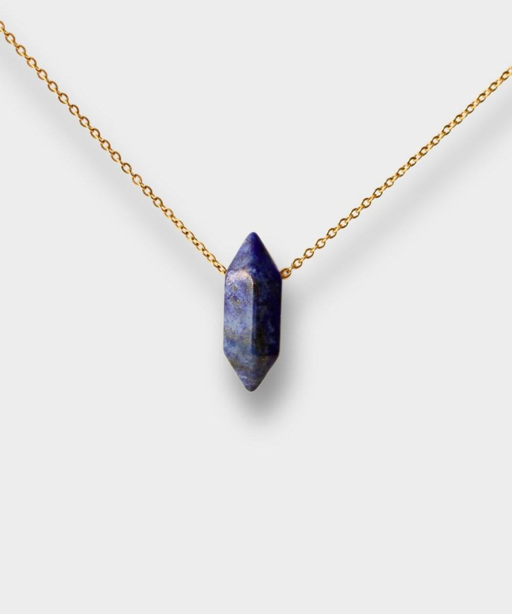 Natural Lapis lazuli crystal necklace. The necklace features a pointed lapis lazuli crystal pendant with a deep blue color and golden flecks. The crystal is attached to a gold chain, creating a stunning and eye-catching piece of jewelry.