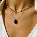 Lapis lazuli crystal necklace. The first necklace features a pointed lapis lazuli crystal pendant, while the second necklace features a delicate gold paper clip chain. Together, the necklaces create a stunning layered look that adds sophistication and elegance to any outfit.