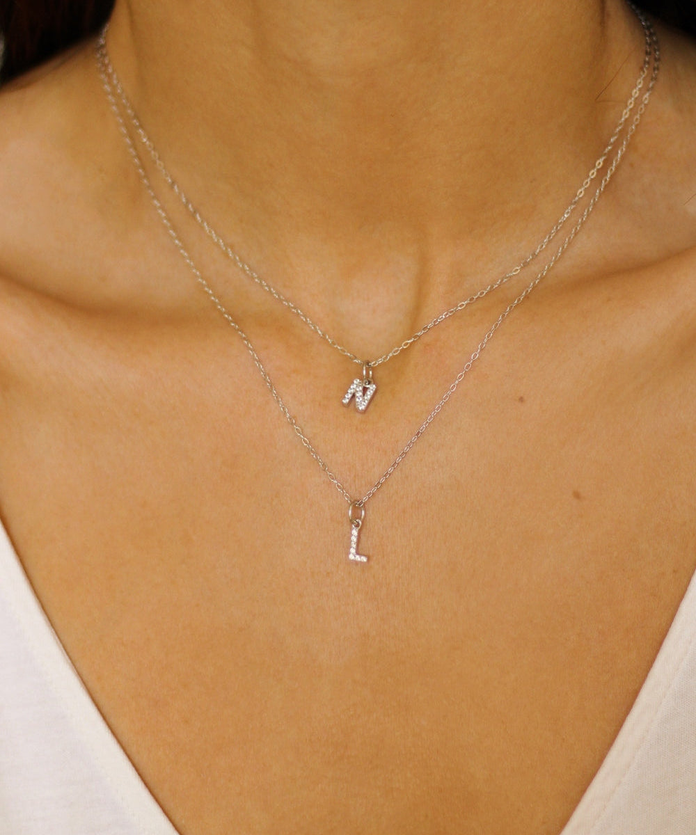 An initial pendant necklace in sterling silver. The necklace features a delicate silver chain, with a pendant in the shape of a single letter L and N from the alphabet. The pendant is intricately designed, showcasing the initial with a stylish and elegant font. Perfect for gifting or adding a personal touch to any outfit.