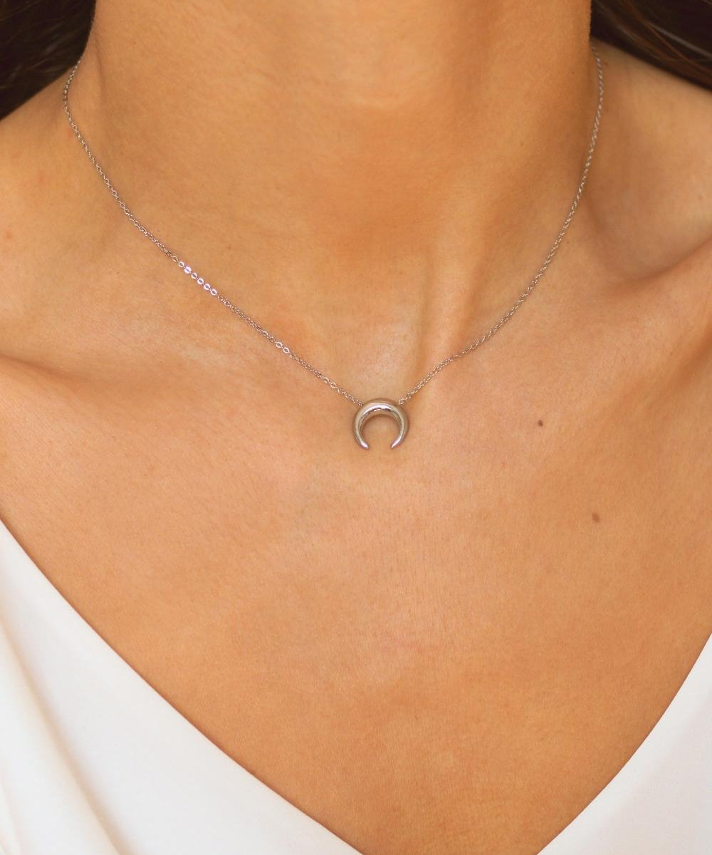 A moon necklace in sterling silver. The necklace features a delicate silver chain with a pendant in the shape of a crescent moon. The necklace is perfect for those who love celestial-inspired jewelry, and makes for an elegant and stylish accessory that can be worn on any occasion.