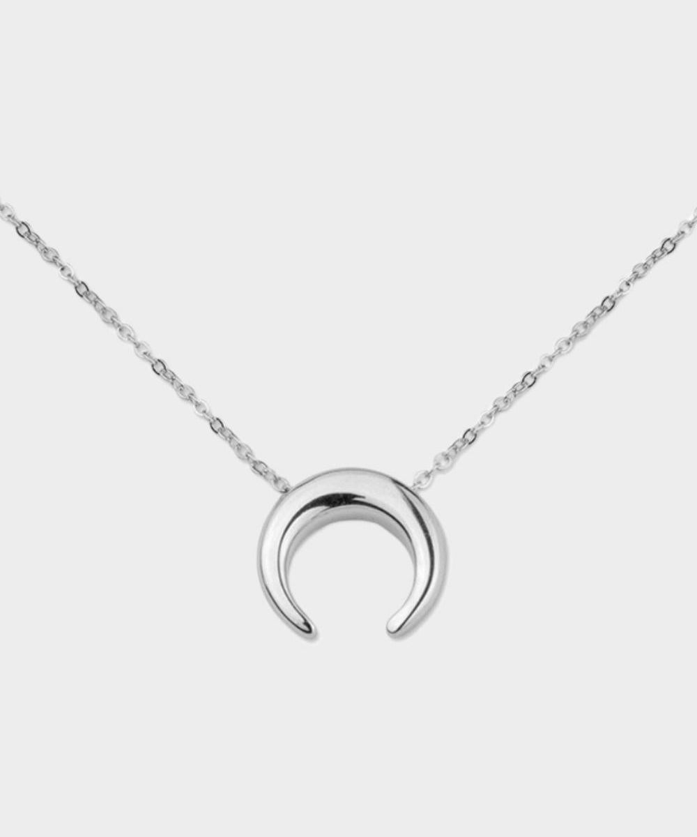 A moon necklace in sterling silver. The necklace features a delicate silver chain with a pendant in the shape of a crescent moon. The necklace is perfect for those who love celestial-inspired jewelry, and makes for an elegant and stylish accessory that can be worn on any occasion.